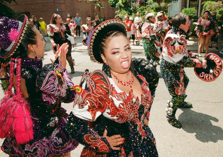 A member of the San Simón Sucre troupe complains about the heat. Queens, NYC. 2024.